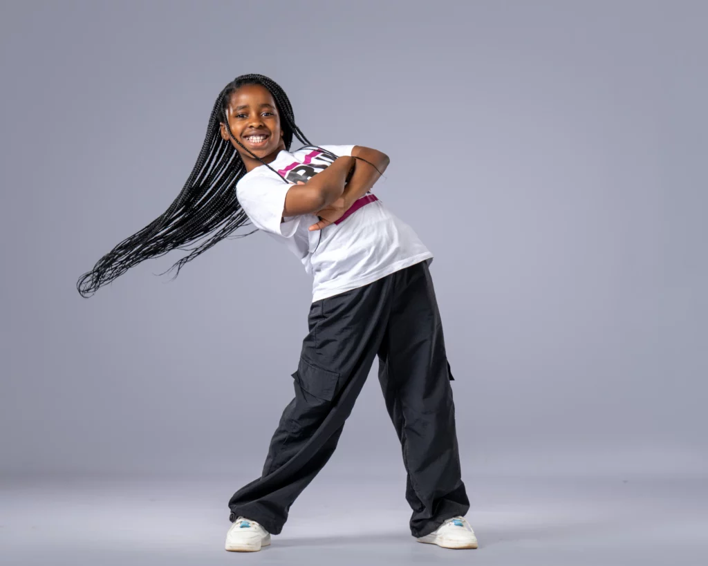 Smiling young girl with long braids posing in a dynamic hip hop stance, representing junior hip hop classes in Johannesburg.