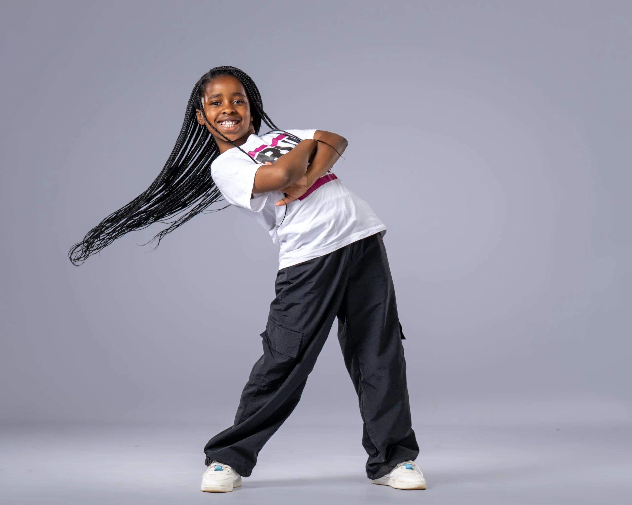 Smiling young girl with long braids posing in a dynamic hip hop stance, representing junior hip hop classes in Johannesburg.